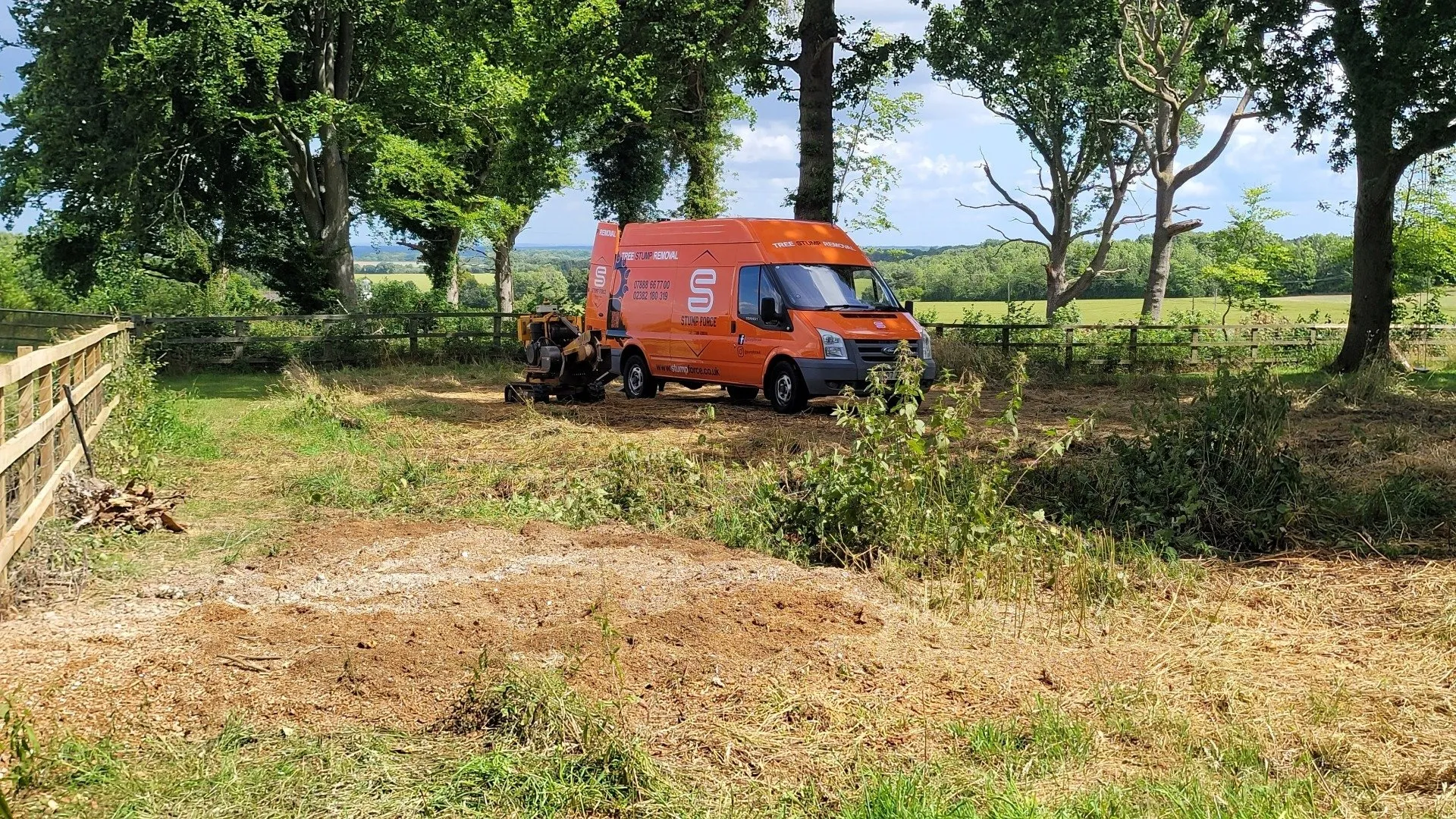 Stump Force van and stump grinding machine in a rural field, with trees and open landscape in the background.