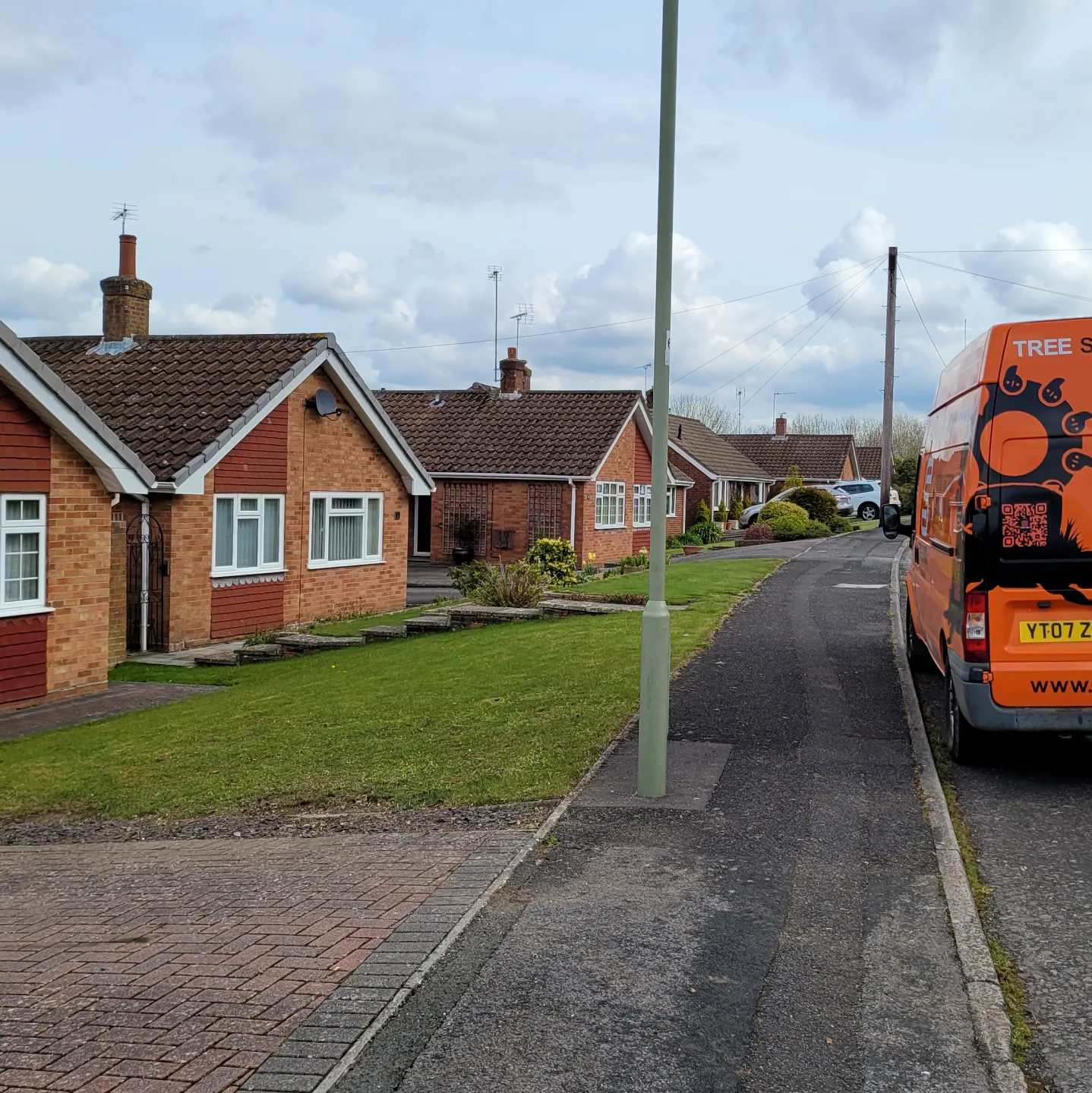 Stump Force van parked along a residential street with red-brick houses on a cloudy day after hedge and stump has been removed.
