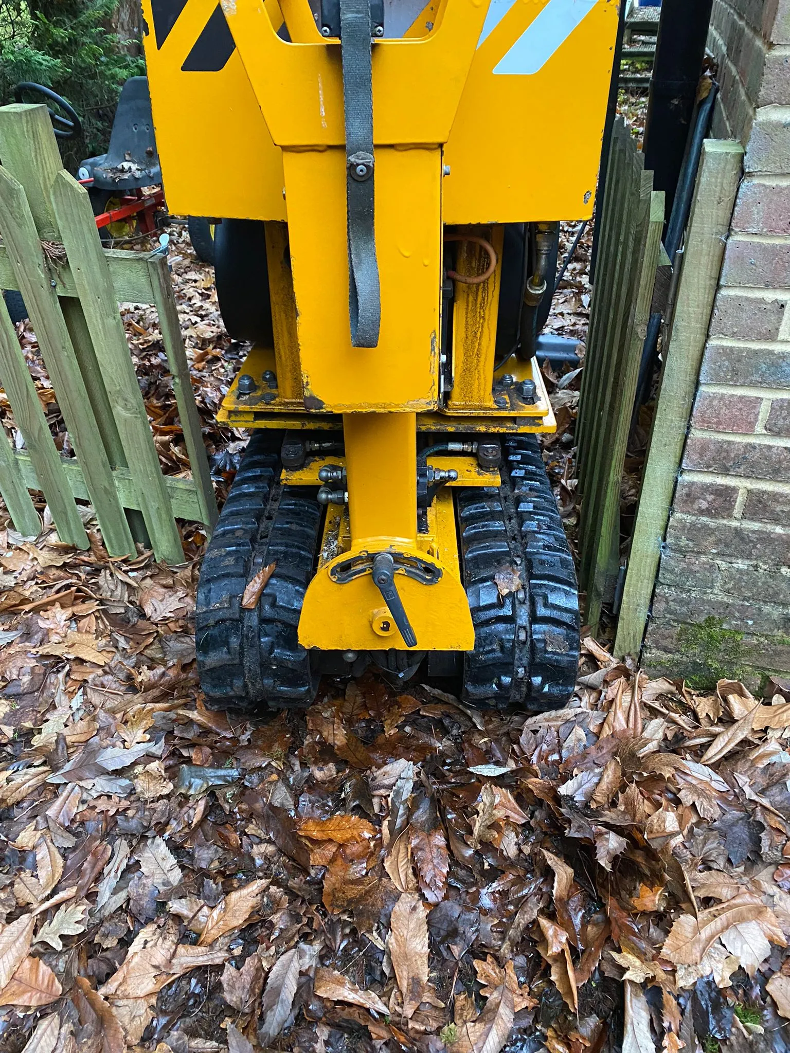 Close-up of tracked wheels on a yellow stump grinder machine navigating a narrow pathway covered with fallen leaves.